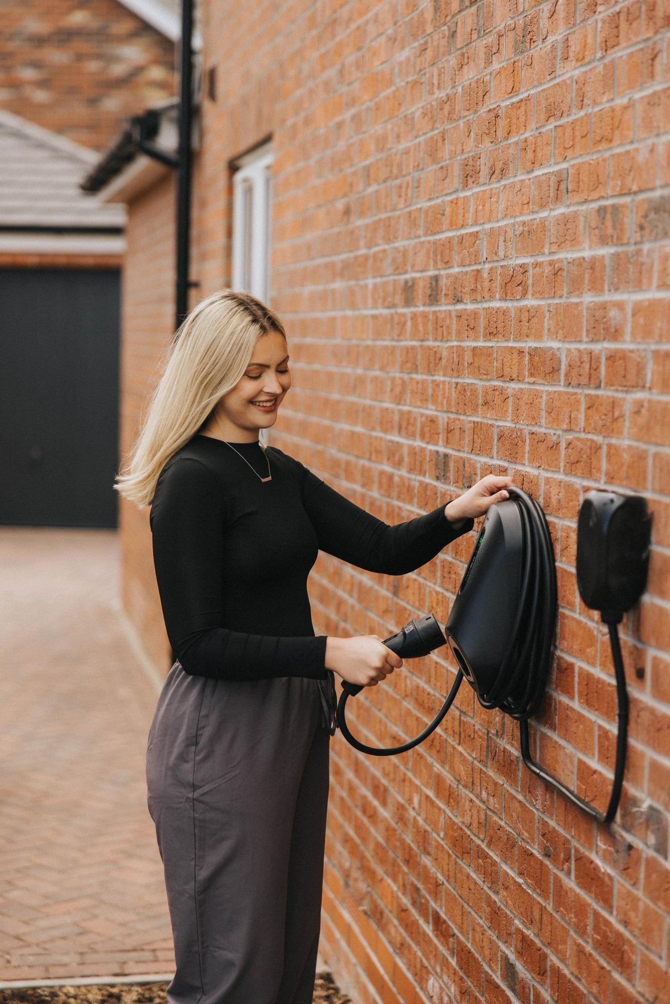 woman plugging cable into wall-mounted electric car charger
