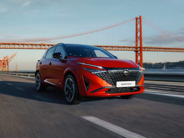 Nissan Qashqai SUV in red driving in front of a bridge